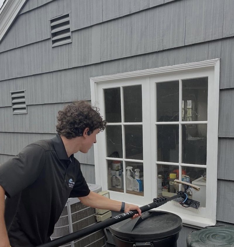 Pacific Pro team member in a branded polo cleaning a window with a water-fed pole