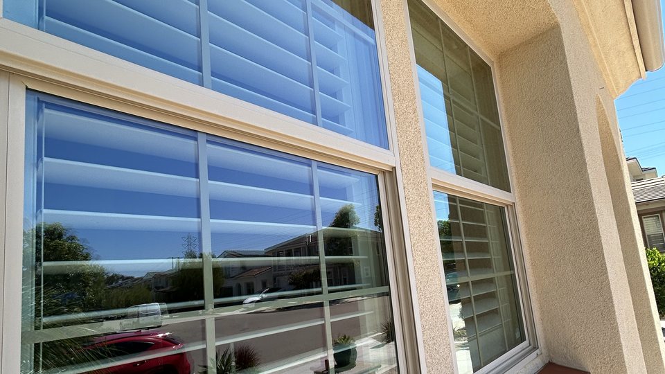 Water-fed brush cleaning a second-storey window on a San Diego home, water running down the glass