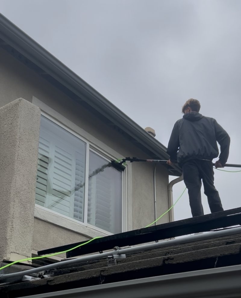 Water-fed brush cleaning a second-storey window on a San Diego home, water running down the glass
