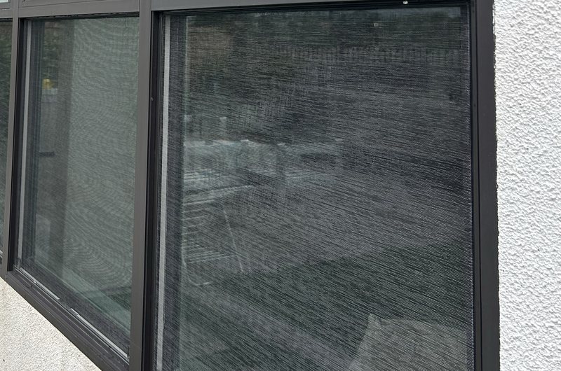 Close view of a dusty window screen before cleaning, showing built-up film across the mesh